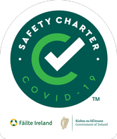 Green circular badge with a white checkmark and text reading SAFETY CHARTER COVID-19. Logos for Fáilte Ireland and the Government of Ireland are at the bottom.